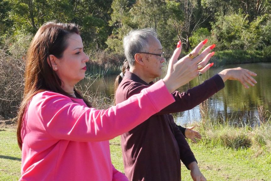 A woman and a man do tai chi in the park
