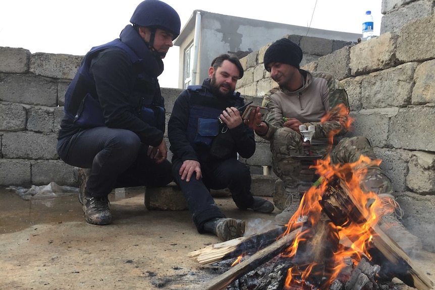 Brown and Hollett with a man in front of camp fire.