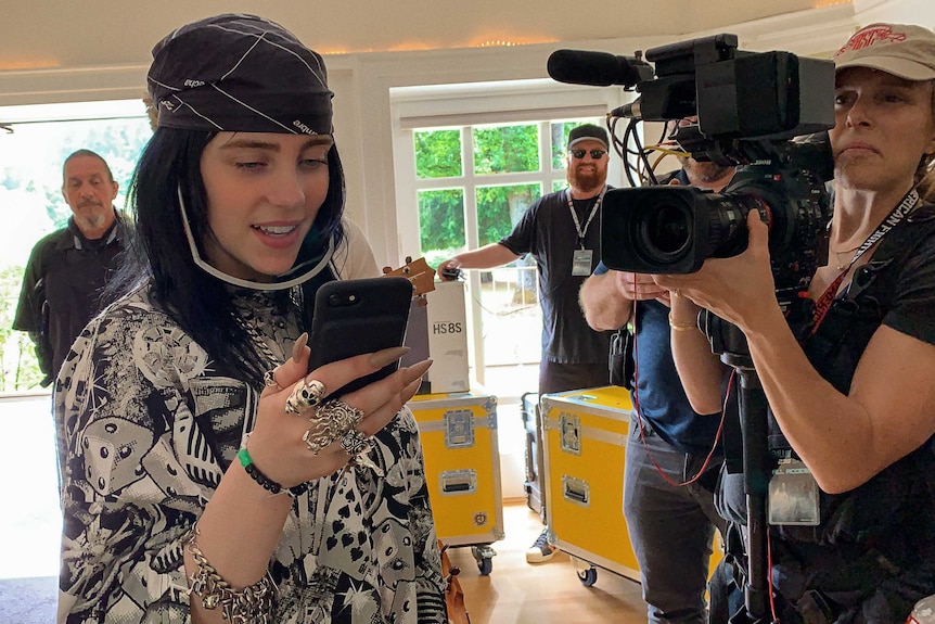 A scene from the documentary  Billie Eilish: The World's a Little Blurry with Billie on her phone, camera woman next to her