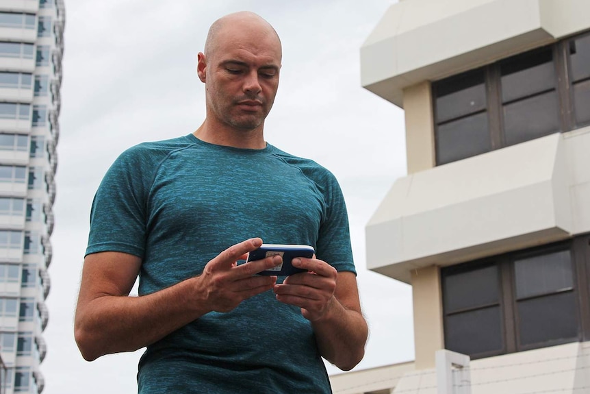 A fit, bald man, wers a turquoise t-shirt, holds a handheld receiver.