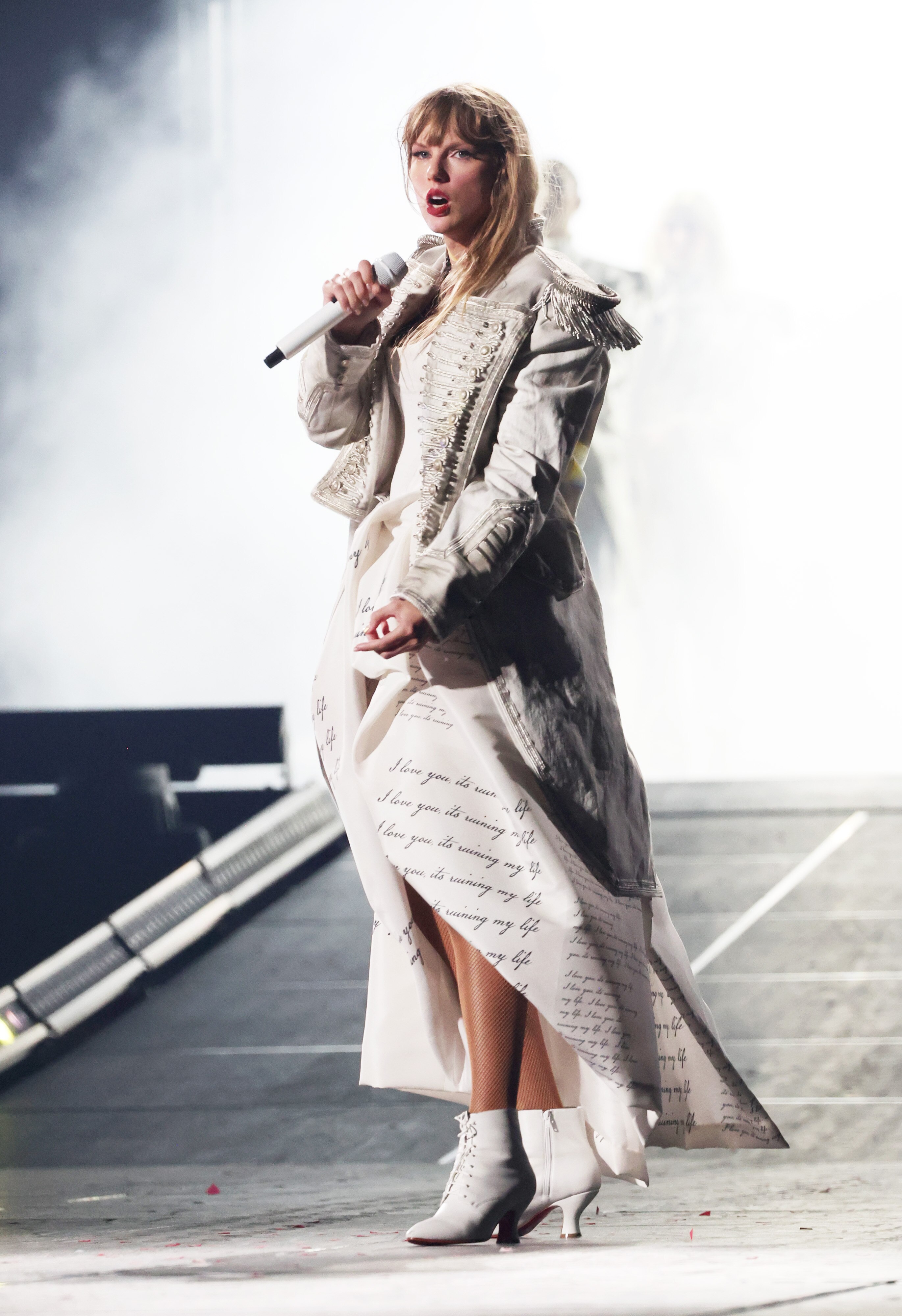 Talyor Swift singing in a white dress and a white leather military jacket 