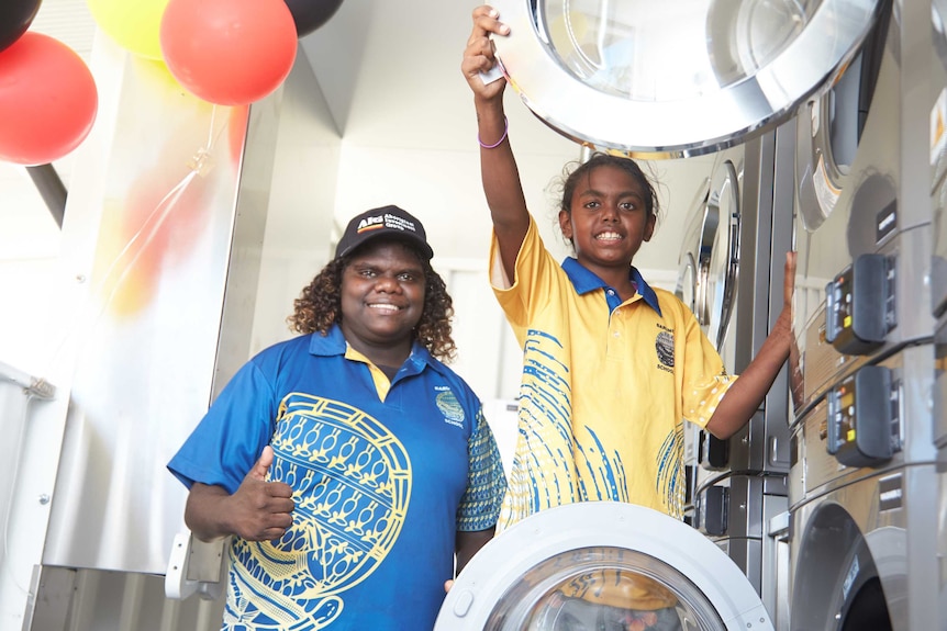 Two kids beside some washing machines.