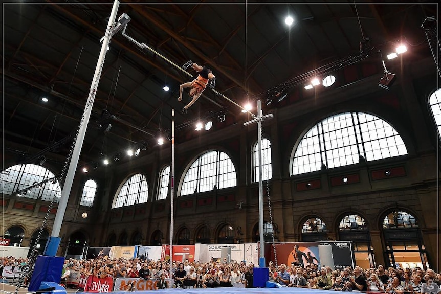 A low shot of Australian pole vaulter Kurtis Marschall clearing the bar at an indoor competition with the crowd behind him.