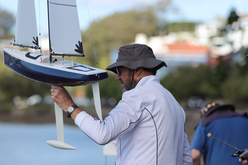 A man with a hat holds a radio-controlled boat.