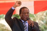 Emmerson Mnangagwa raises his arm with a clenched fist while speaking into a microphone.