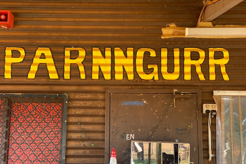 A brightly coloured sign that says "Parnngurr", painted on a tin wall.