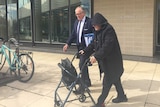 John chute (R) uses a walking frame outside the court building.