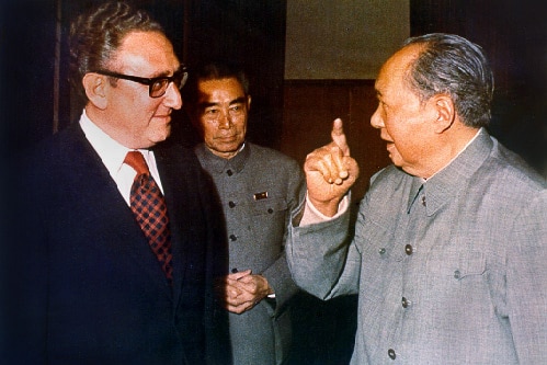 Henry Kissinger stands next to Chairman Mao with a third man in the background.