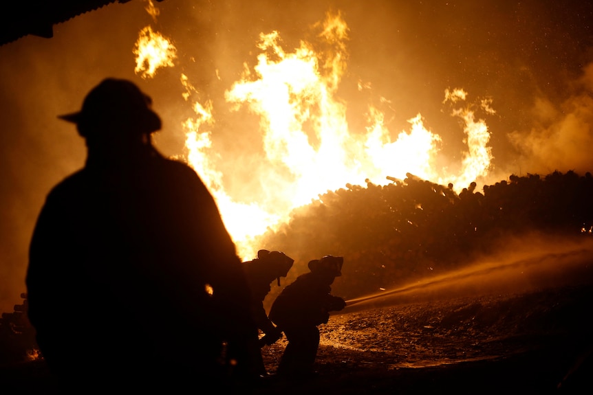 Firefighters are silhouetted against raging orange flames 