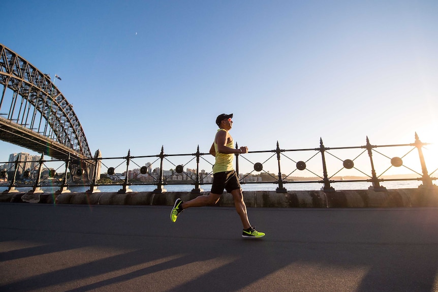 A man runs along the foreshore of Sydney Harbour with the Harbour Bridge in the background