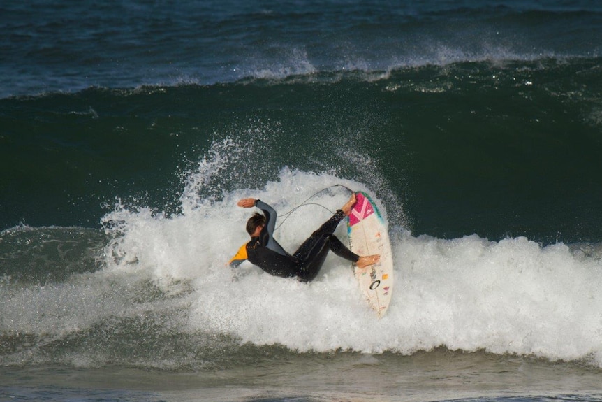 A surfer doing a turn on a broken wave, with a larger wave rising behind him.