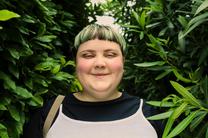 A woman with short green and black hair smiles amongst a field of plants