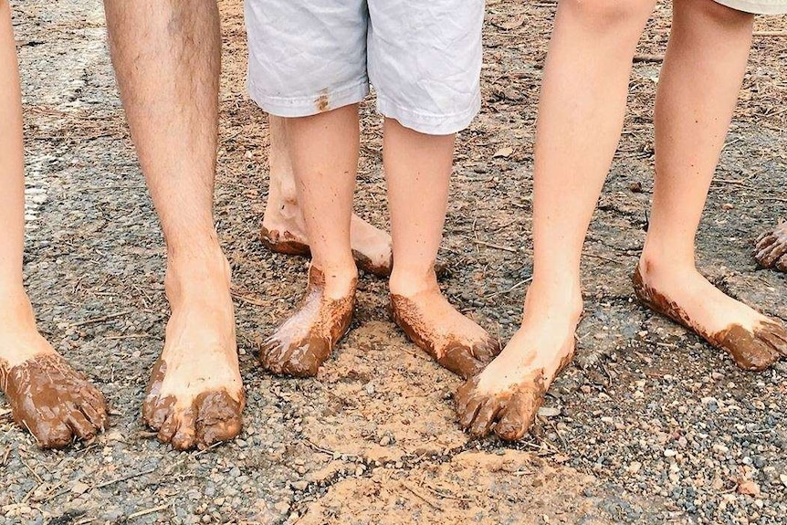 Six people with mud on their feet and shows stand side by side on dirt.