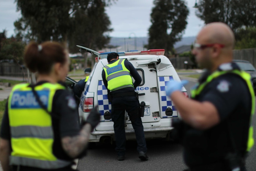 A police officer secures the rear door of a police van as two other officers look on.