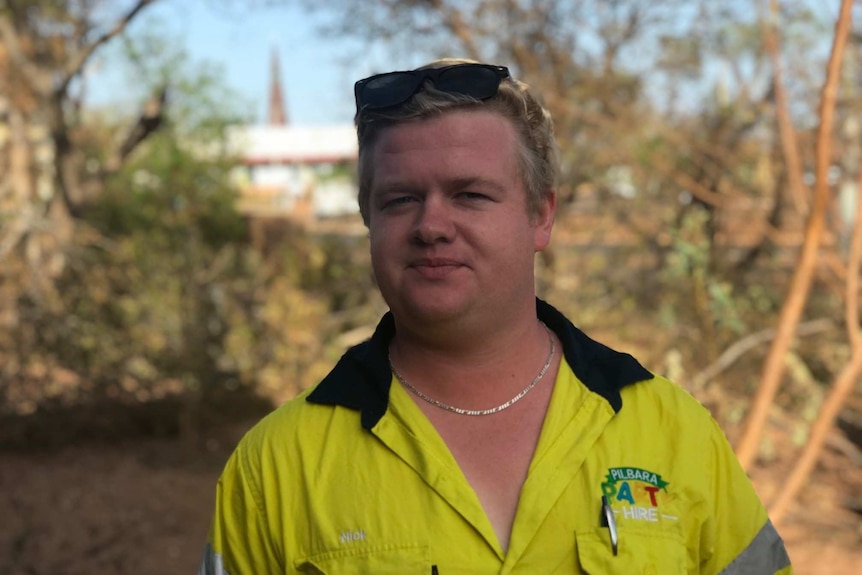 A man in a high-vis shirt with sunglasses on his head smiles at the camera.