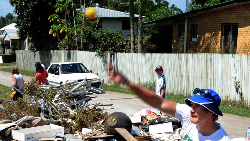 Shane Watson bowls during a game of street cricket amongst flood debris