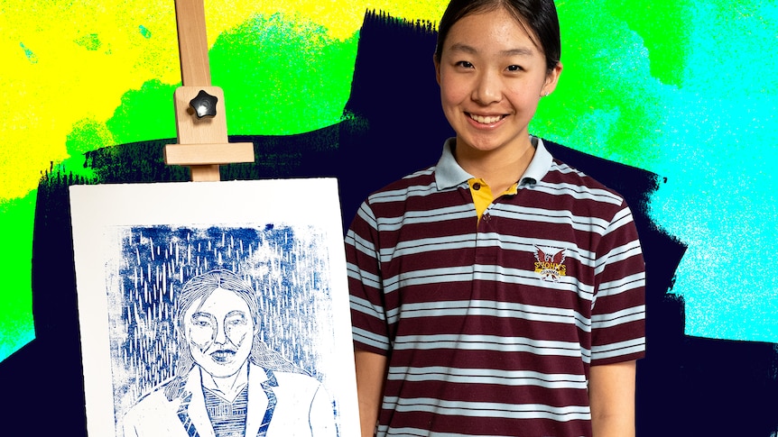 Lexie smiles while standing next to her woodcut self portrait propped up on an easel.