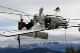 The light plane hangs upside down in the cables with a rescuer and the passenger on the wing.