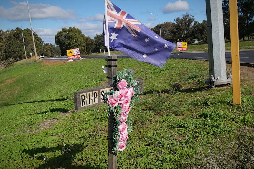 A cross adorned with flowers sits on a highway road side