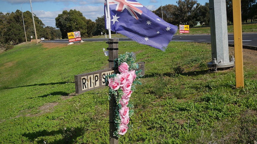 A cross adorned with flowers sits on a highway road side