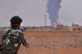 A YPG fighter watches smoke billowing in the Syrian city of Hasakeh
