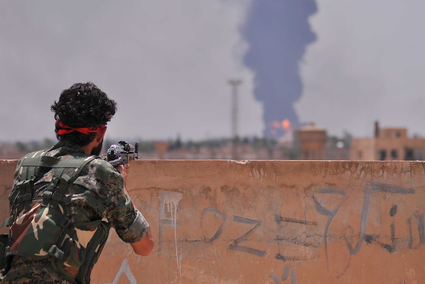 A YPG fighter watches smoke billowing in the Syrian city of Hasakeh