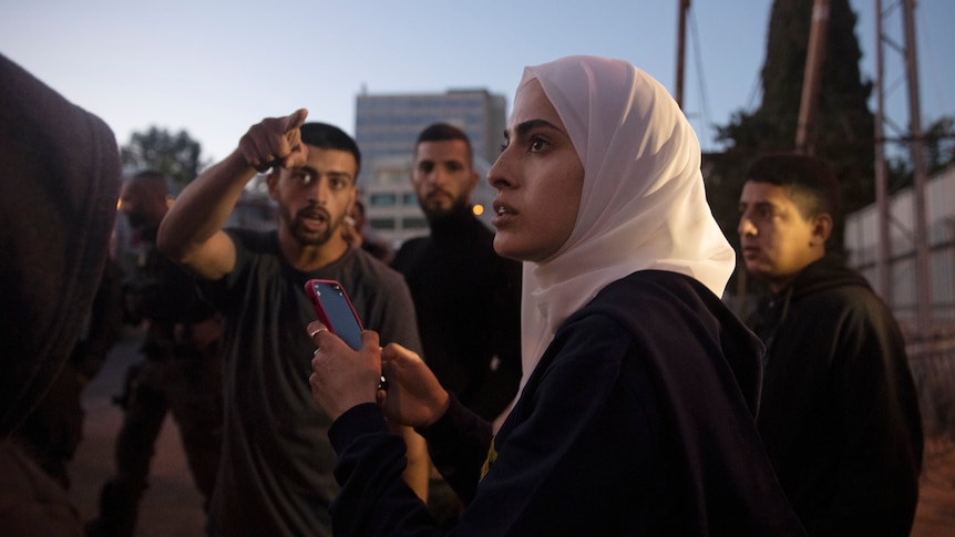 A woman wearing a hijab holds a phone.