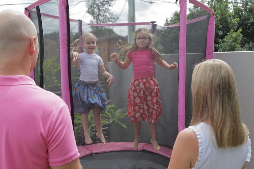 Two children jump on a trampoline while their parents watch.