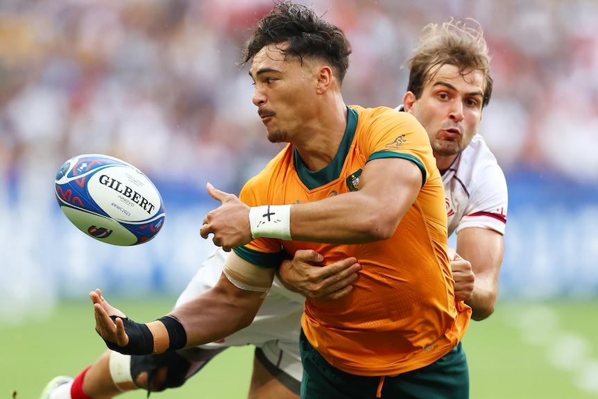 A Wallabies player passes the ball to his right while being tackled by a Georgian opponent at the 2023 Rugby World Cup.