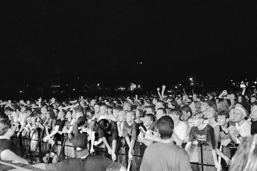 The view of a crowd from a stage with people packed against a metal barrier
