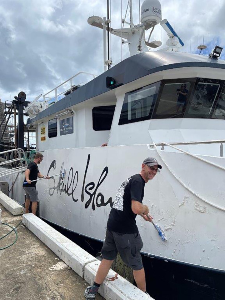 Two men painting a boat at dock.