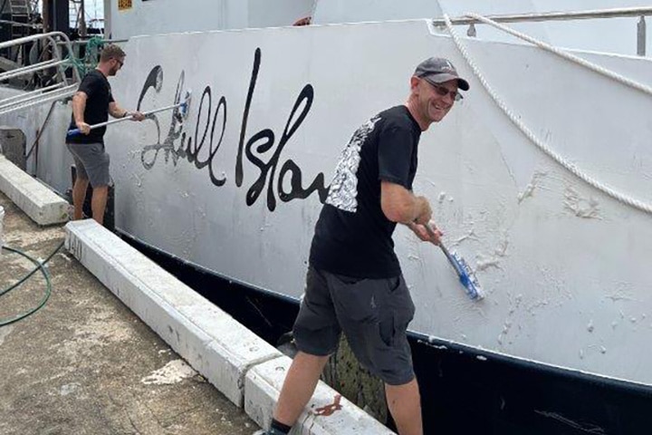 Two men painting a boat at dock.