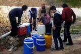 A frame grab from a video shows men and children filling buckets and containers with water on the side of the road.