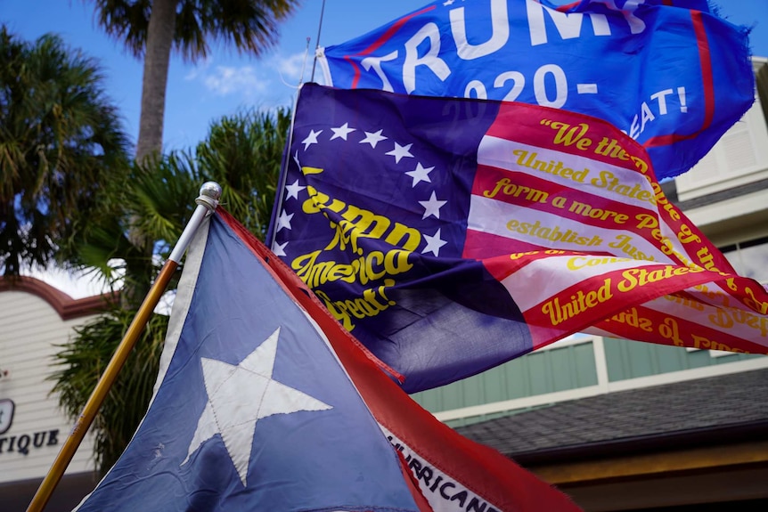 Red, white and blue flags with Trump 2020 written on it sway in the air.