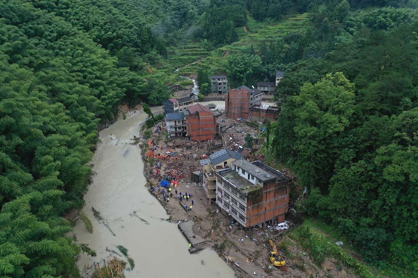 Aerial photo shows town with river surrounded by forest, with damaged buildings from landslide.