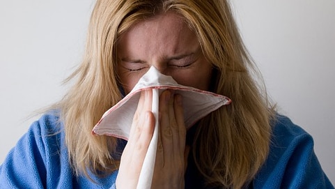 Woman sneezing into handkerchief.