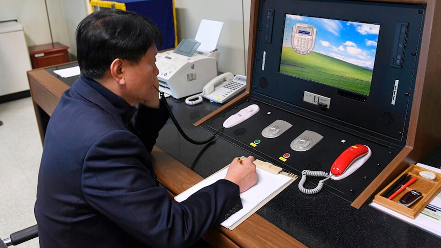 A middle aged man in a suit uses a phone and a computer built into a specialised communications desk.