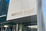 The exterior of the WA District Court building, with signage and glass doors, with steel artwork out the front.