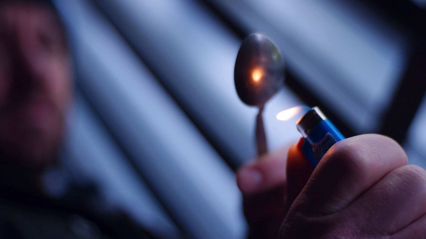 An unidentifiable man holds a spoon above a lighter