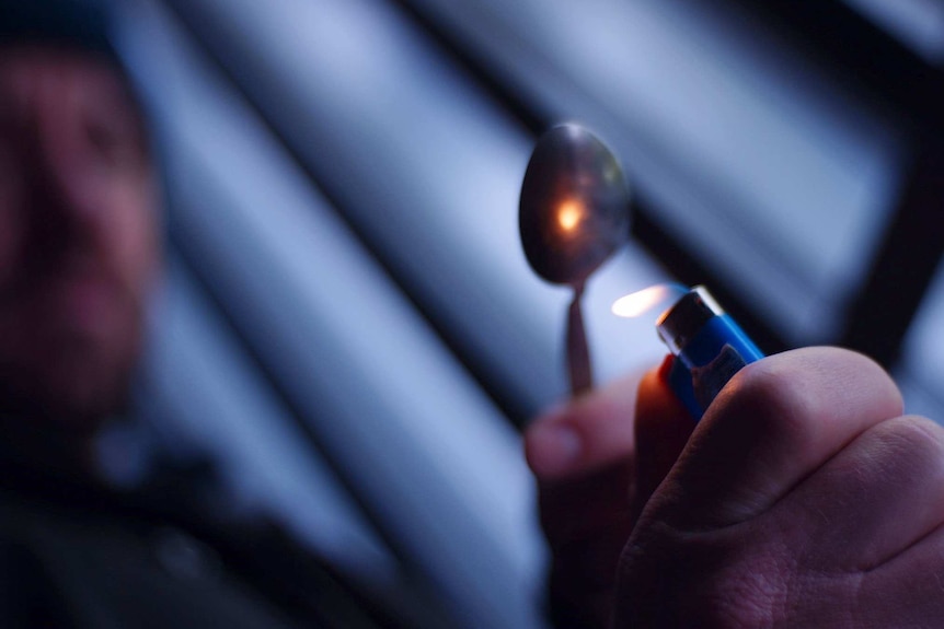 An unidentifiable man holds a spoon above a lighter