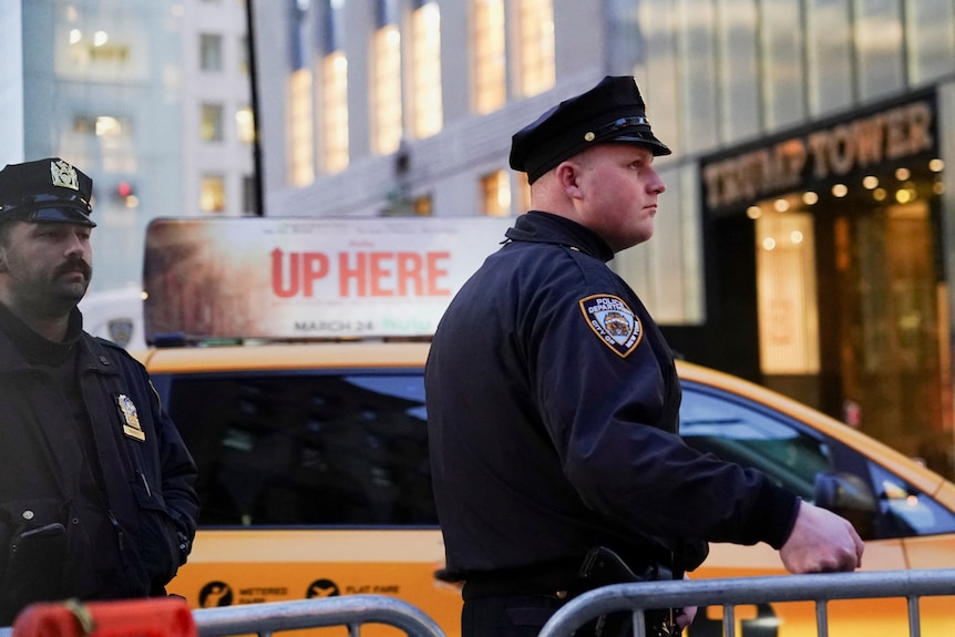 Two police officers wearing hats stand by a barricade next to a yellow cab outside Trump Tower