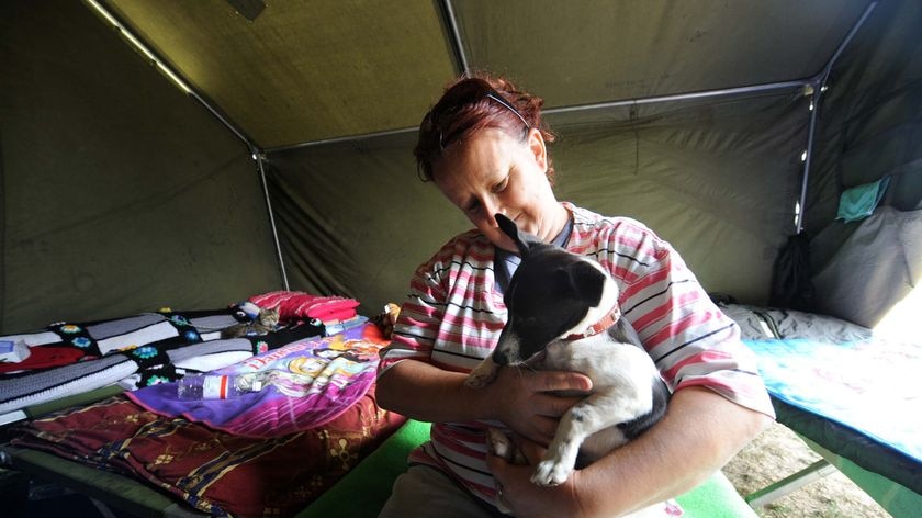 A woman hugs her dog as she sits in an emergency shelter