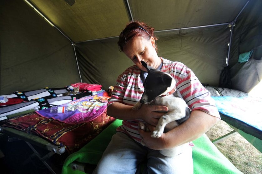 A woman hugs her dog as she sits in an emergency shelter