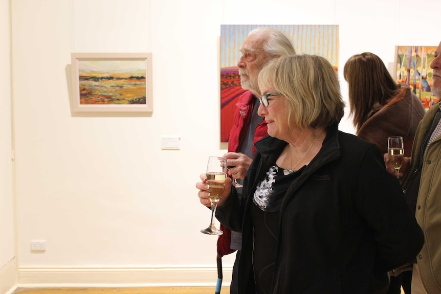 A woman with short blonde hair smiles at a painting at the Pro Hart Outback Art Prize exhibition.