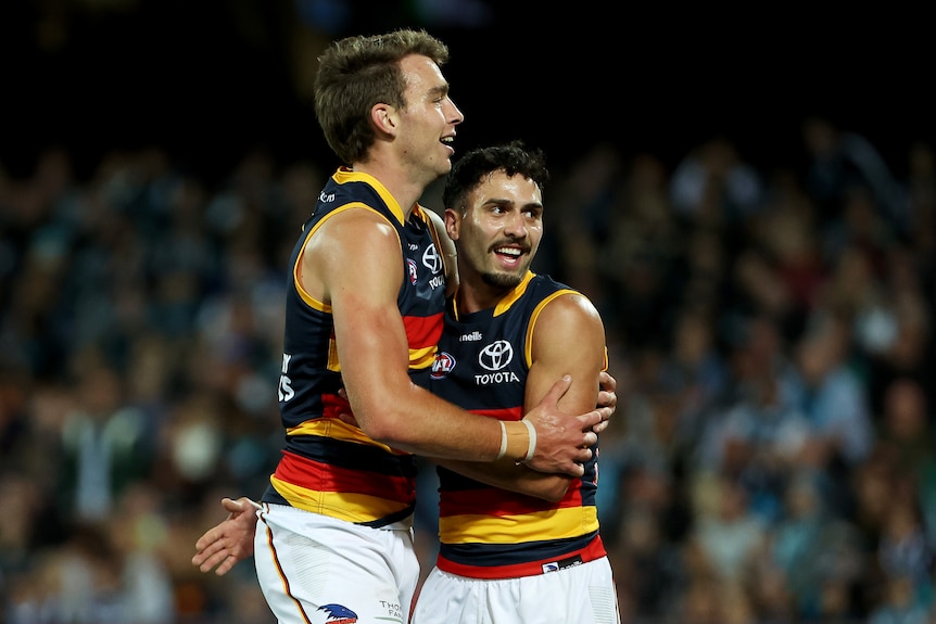 Two Adelaide Crows players hug after kicking a goal.