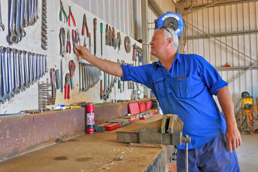 A man replaces a tool on the wall of his work shed