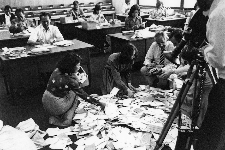Radio Australia receives its weekly mail in 1969. Envelopes are all over the mail room floor, and staff appear very busy.