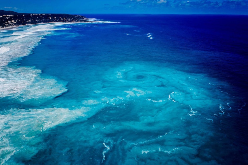 An aerial shot of a strikingly blue sea with a huge vortex out past the breakers.