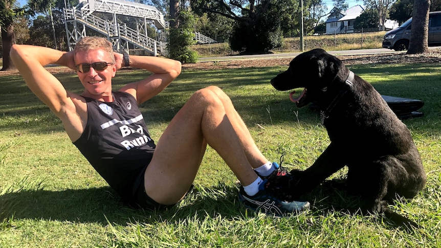 blind runner gerrard gosens does a sit-up with a black dog leaning its front paws on his feet