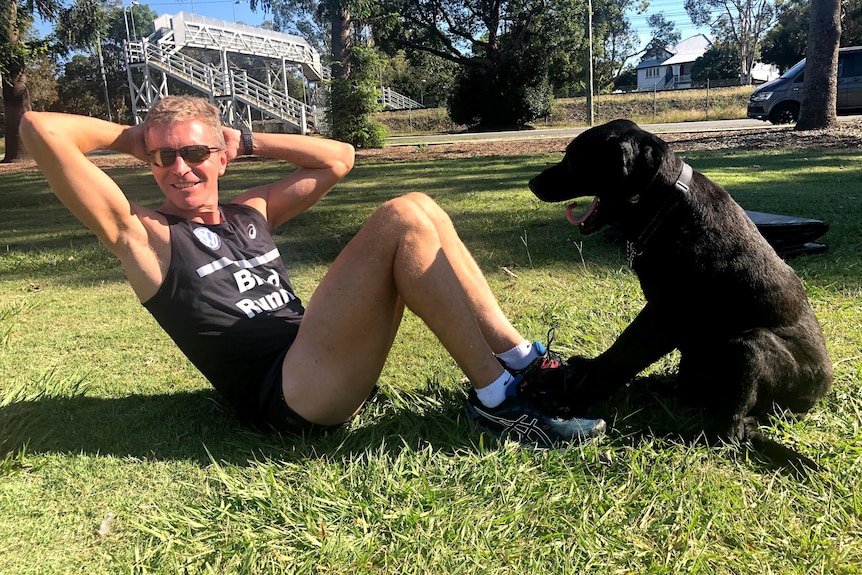 blind runner gerrard gosens does a sit-up with a black dog leaning its front paws on his feet